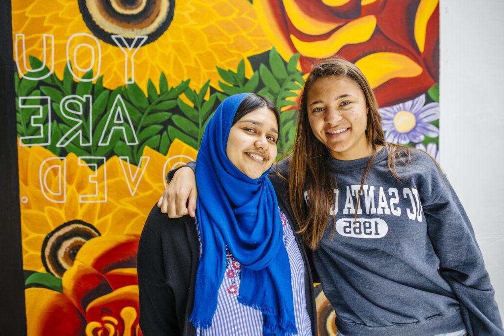 Two student smiling in front of a mural