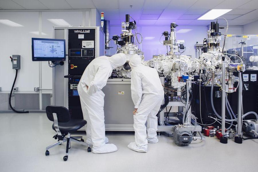 Two scientists in a clean room with white jumpsuits on observing and experiment.