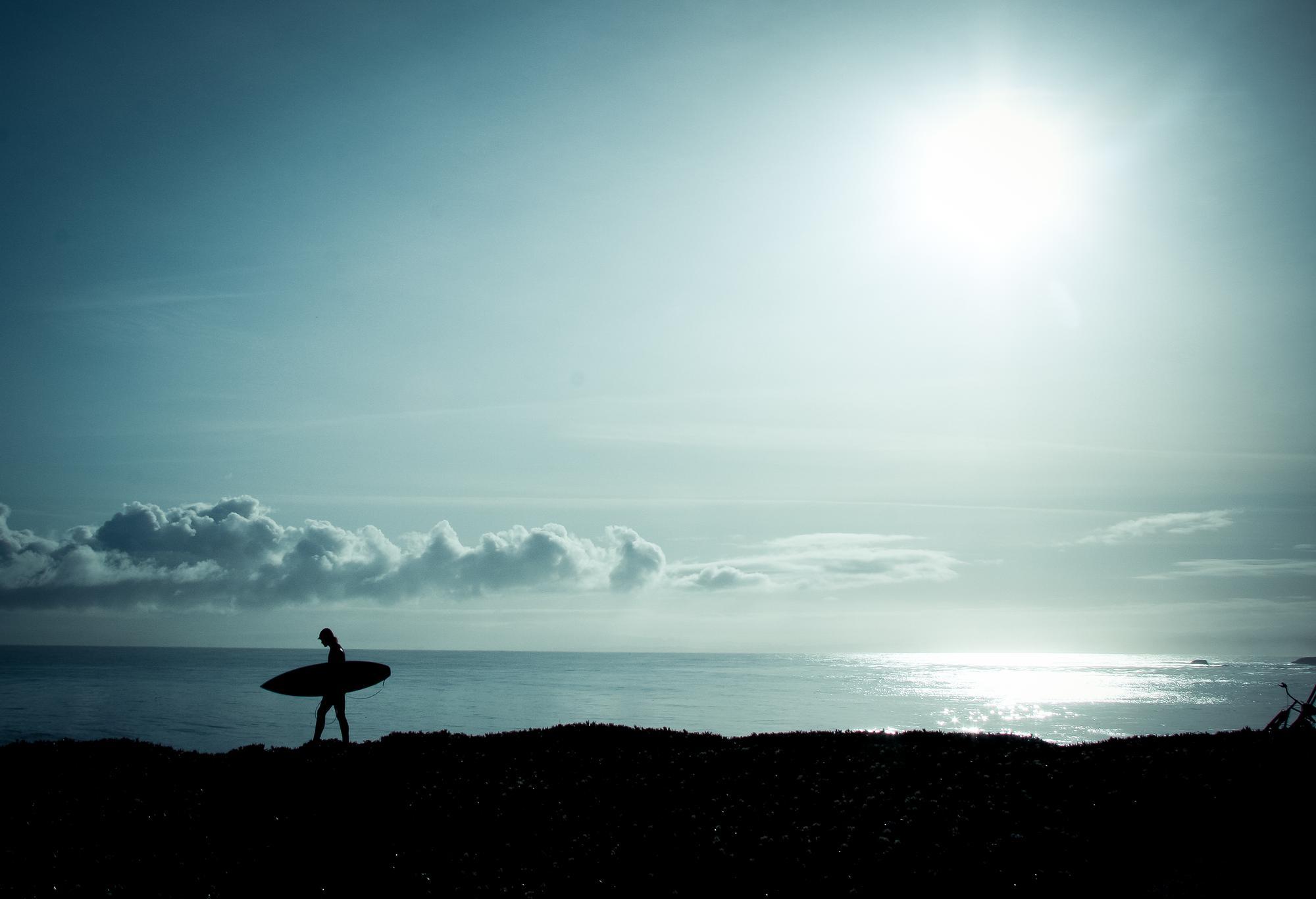 Silhouette of person walking by the ocean with a surf board